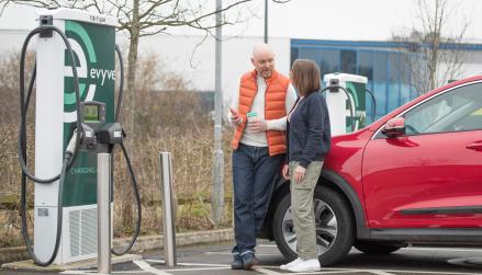 Evyve charge points being used by two people leaning on EV using Zapmap on their mobile phone