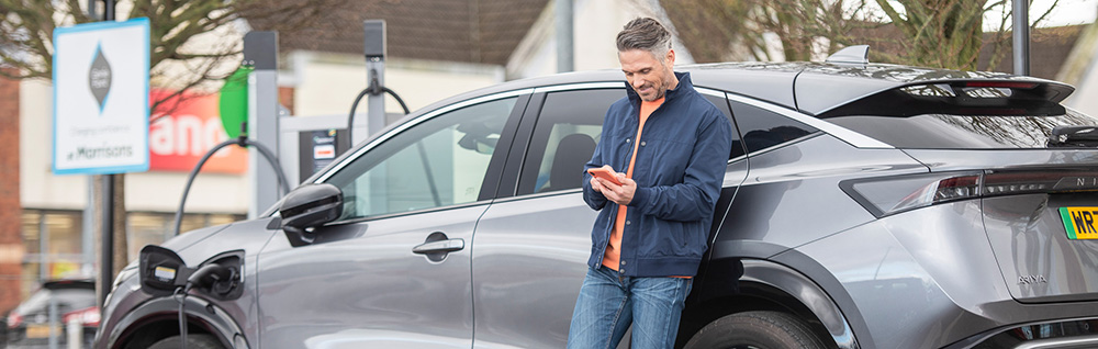 Man charging EV in car park while using Zapmap on his phone