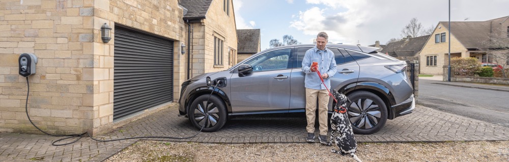 Man and dog stood next to car on charge