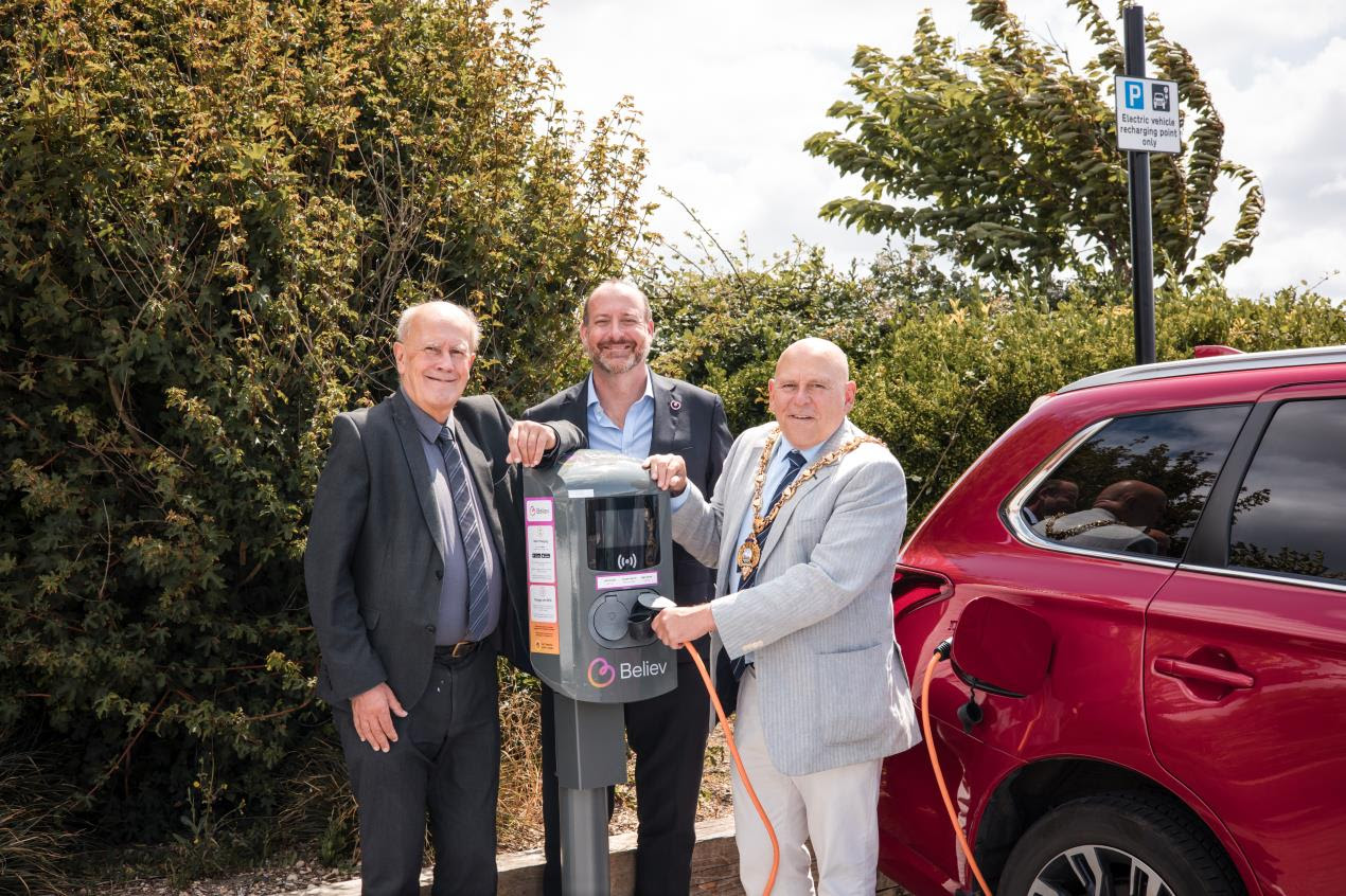 Council members stand next to a Believ charge point plugged into a red EV