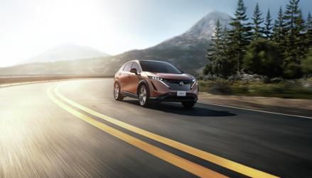 Nissan Ariya driving on road with mountains and forest in background