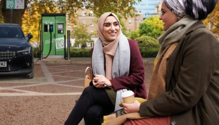 Two women in foreground, Be.EV charge point and EV in background