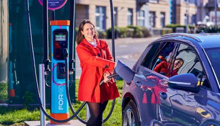 FOR:EV charger in use by woman in red coat, charging blue EV