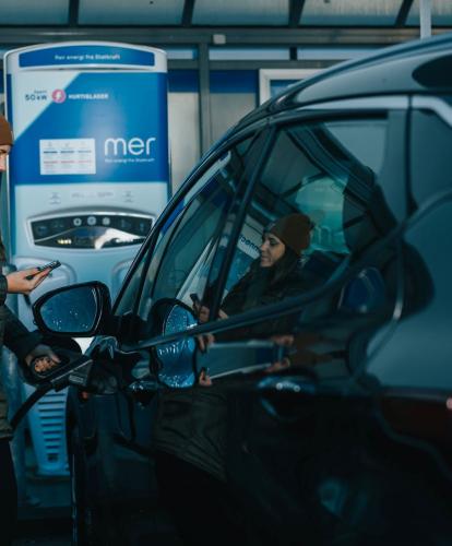 Mer charger - lady with a brown hat chargers her EV while holding phone