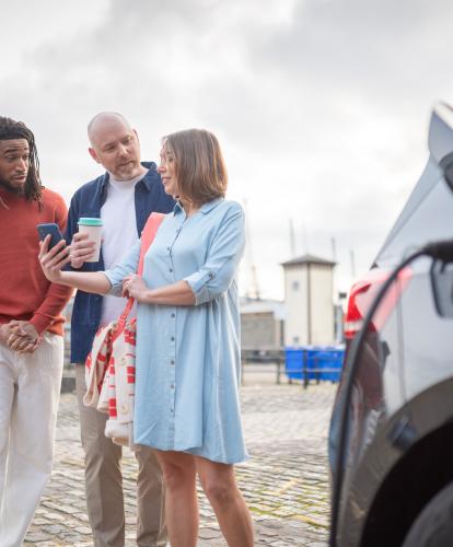 Stock photo - 3 people looking at Zapmap app behind an EV on charge