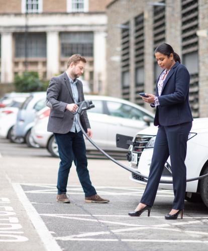 Businessman and businesswoman dressed smartly charging their EV and using the Zapmap app