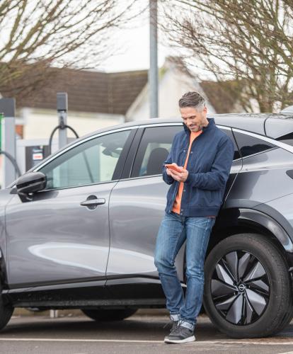 Supermarket charging - man leans against EV while using Zapmap on his phone