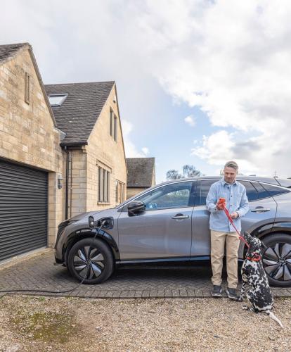 Home charge point charging EV next to man using Zapmap app on phone holding leash of Dalmation dog