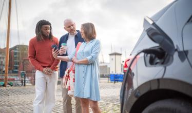 Stock photo - 3 people looking at Zapmap app behind an EV on charge
