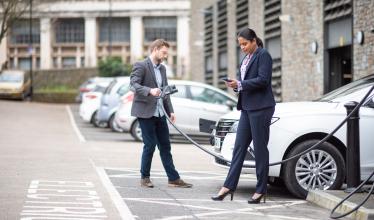 Businessman and businesswoman dressed smartly charging their EV and using the Zapmap app