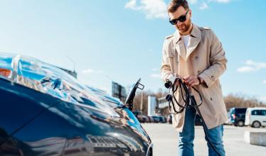 Man holds charging cable in front of EV bonnet